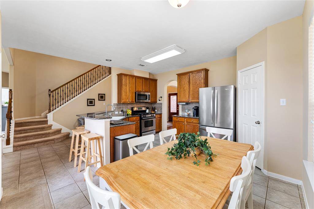 Open kitchen with stainless steel appliances, granite countertops, and tile flooring. Features oak cabinetry, a double basin sink, and a pantry to the right.