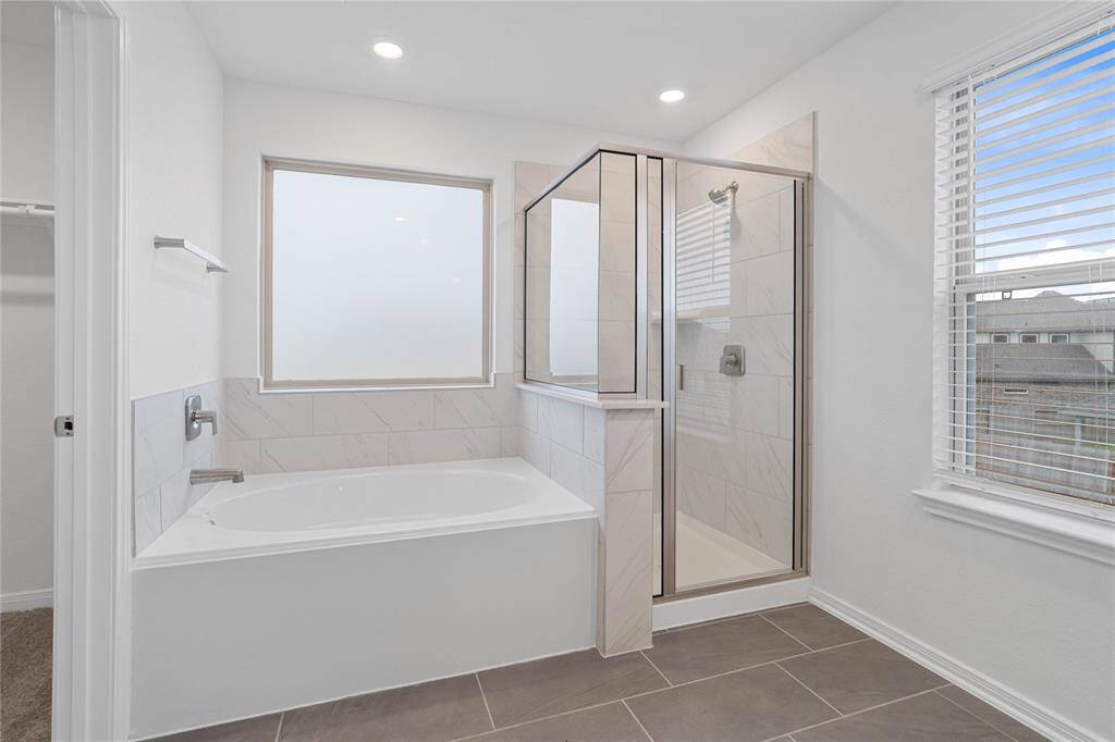 Additional view of the primary bathroom featuring a walk-in shower with tile surround and a garden tub, great for soaking after a long day!