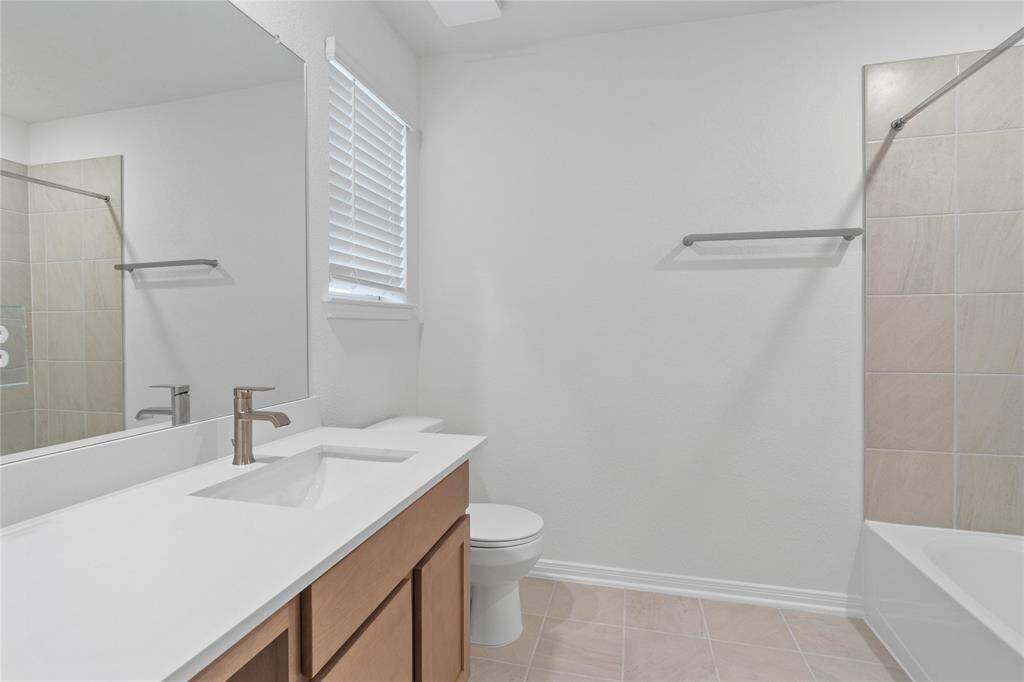 Secondary bath features tile flooring, bath/shower combo with tile surround, stained wood cabinets, beautiful light countertops, mirror, sleek fixtures and modern finishes.