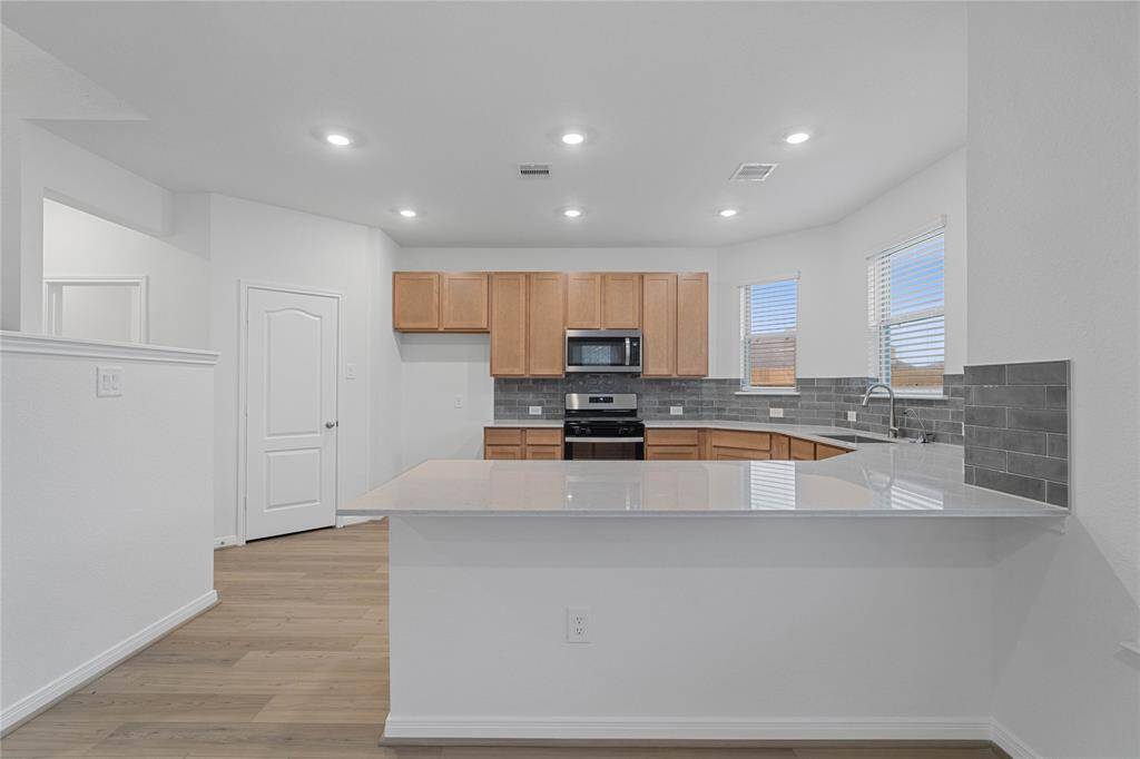 This spacious kitchen features high ceilings, stained wood cabinets, silestone countertops, SS appliances, modern tile backsplash, recessed lighting, space for a breakfast bar, and a pantry all overlooking your huge family room.