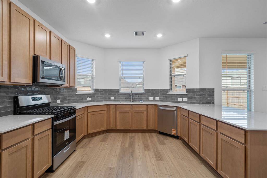This spacious kitchen features high ceilings, stained wood cabinets, silestone countertops, SS appliances, modern tile backsplash, recessed lighting, space for a breakfast bar, and a pantry all overlooking your huge family room.
