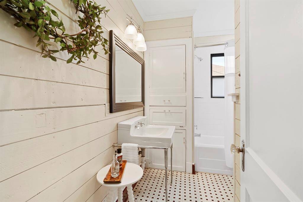 Bright, clean, fully restored full bathroom features built-in storage, shower tub combo, original tile flooring, insulated shiplap walls and window providing natural light.