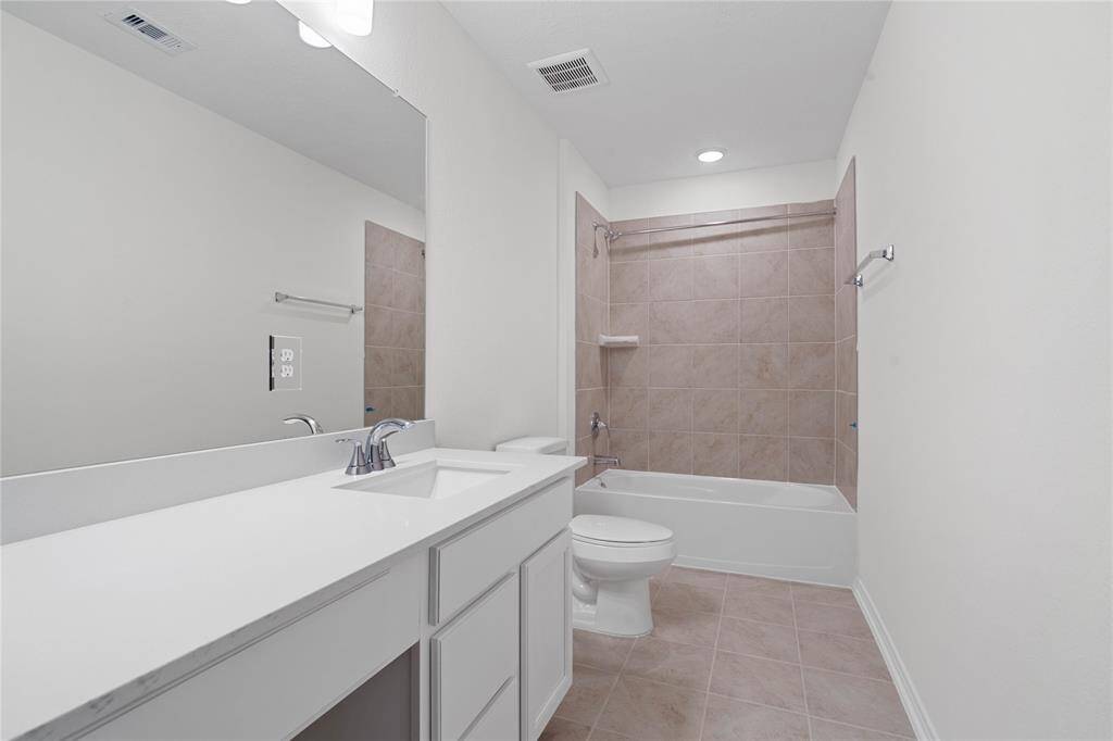 Secondary bath features tile flooring, bath/shower combo with tile surround, stained wood cabinets, beautiful light countertops, mirror, sleek and modern finishes.
