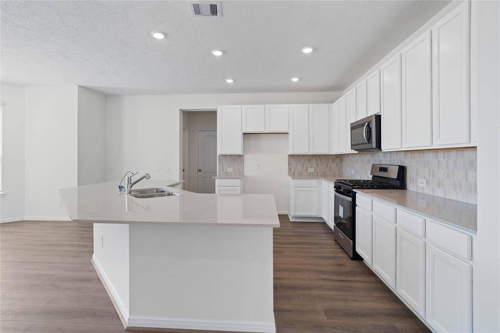 This kitchen will not disappoint! Your family and guests will enjoy many nights of fun, food and entertainment with ample counter space and kitchen island for setting up a wonderful array of provisions! This view of this gorgeous kitchen showcases SS appliances including microwave, silestone countertops, kitchen island with extended countertop to breakfast bar, beautiful tile backsplash, gas range, high ceiling, recessed lighting and tile floors!