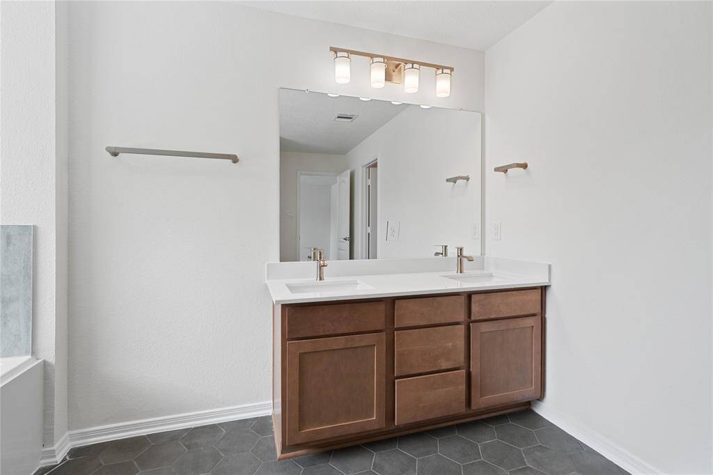 This primary bathroom is definitely move-in ready! Pictured here is the spacious dual vanity area with stained cabinets and light countertops, high ceilings, neutral paint, sleek and modern finishes.