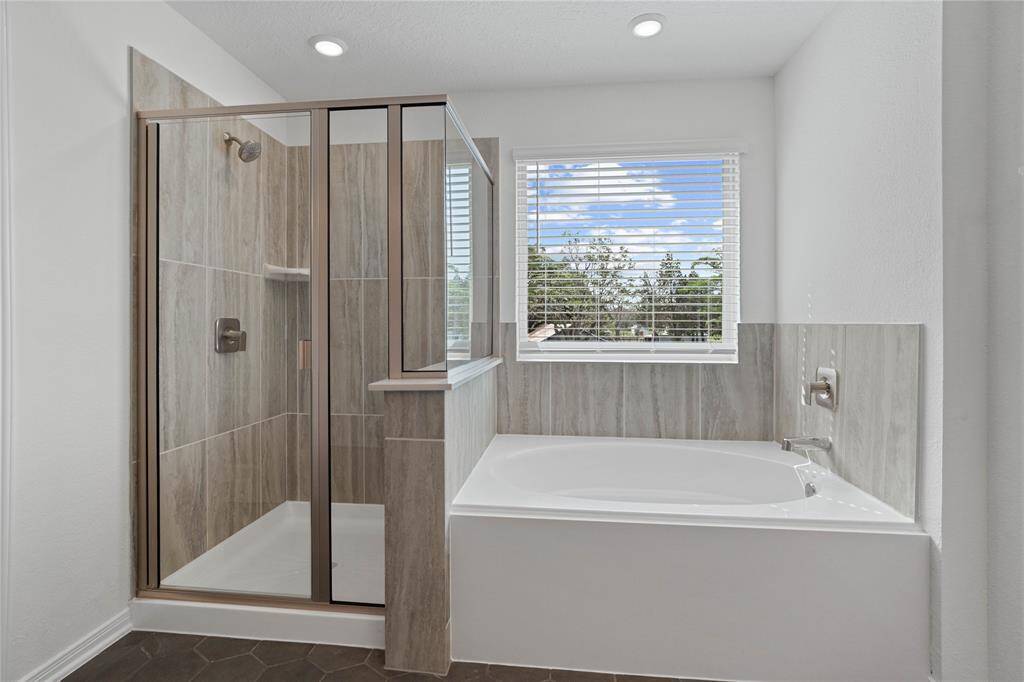 Another view of this primary bathroom features a walk-in shower with tile surround, garden tub, window with blinds, neutral paint, and sleek and modern finishes.