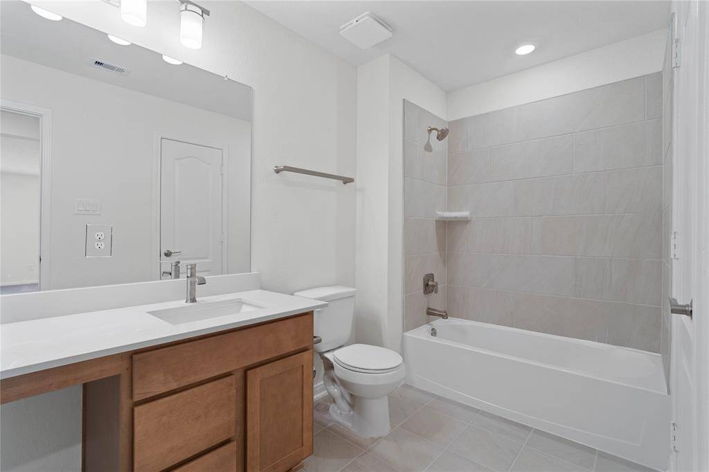 Secondary bath features tile flooring, bath/shower combo with tile surround, stained wood cabinets, beautiful light countertops, mirror, sleek fixtures and modern finishes.