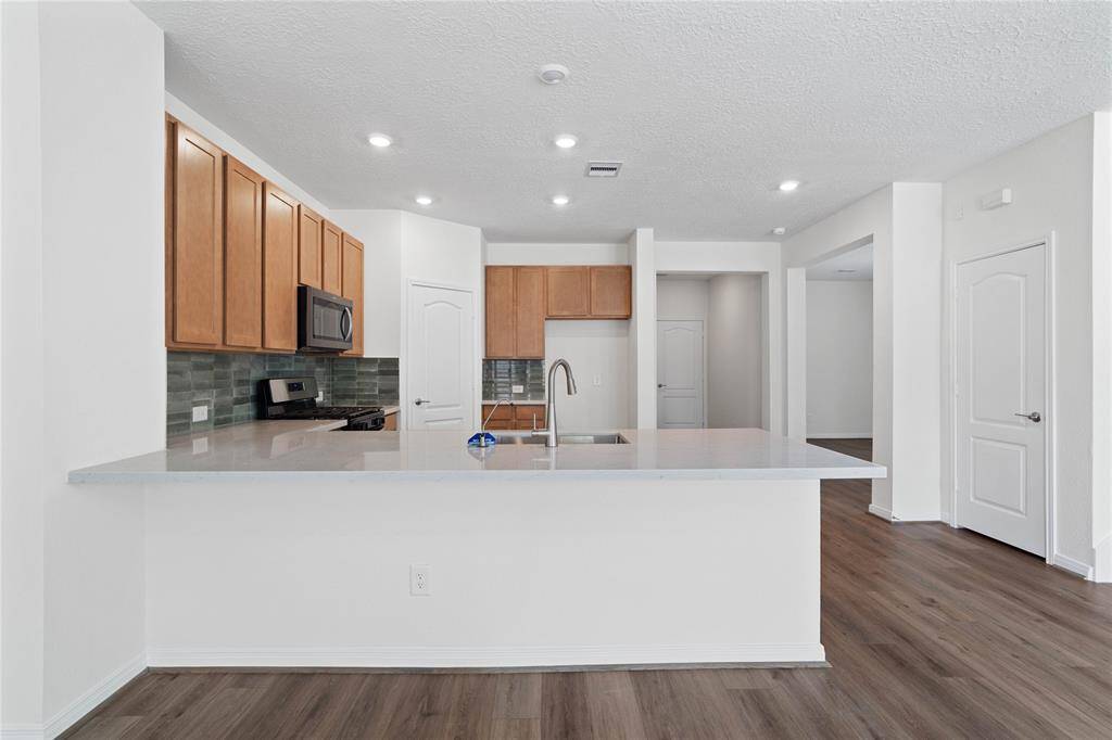 This spacious kitchen features high ceilings, stained wood cabinets, silestone countertops, SS appliances including microwave, modern tile backsplash, recessed lighting, extended countertop for breakfast bar, and a pantry all overlooking your huge family room.