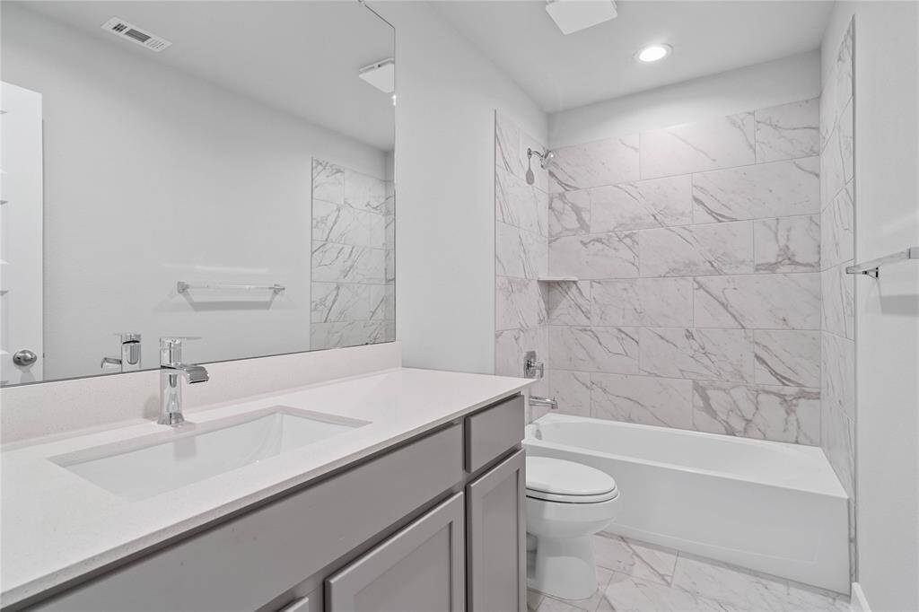 Secondary bath features tile flooring, bath/shower combo with tile surround, stained wood cabinets, beautiful light countertops, mirror, sleek fixtures and modern finishes.