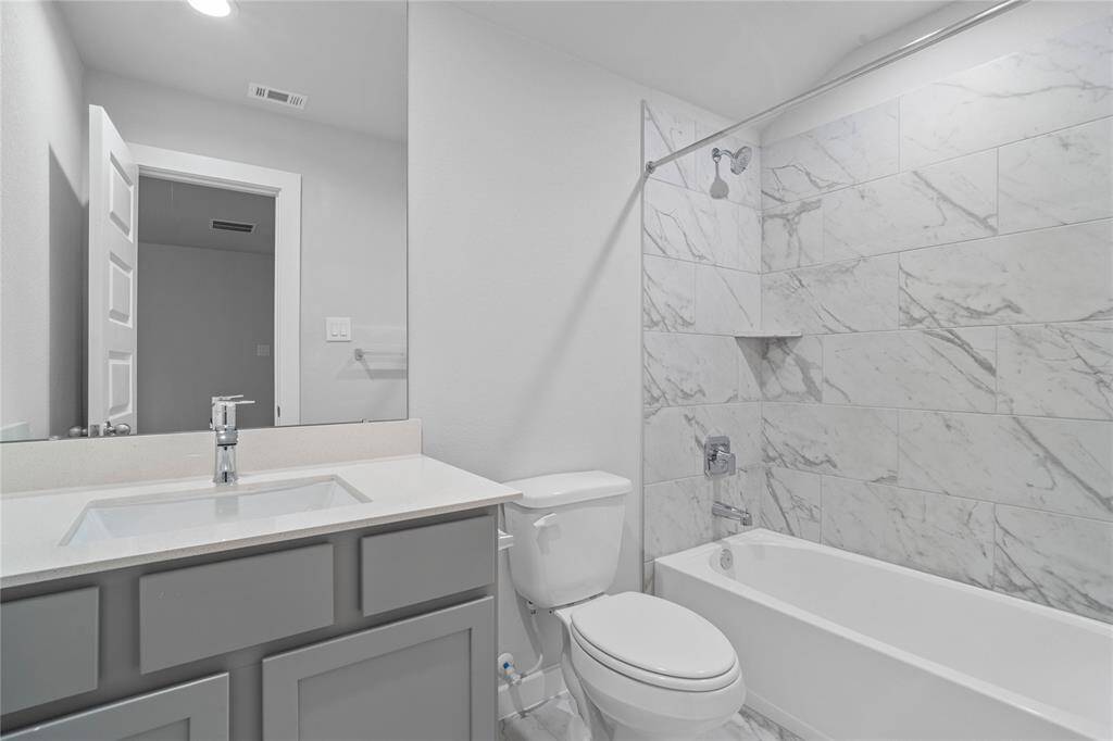 Secondary bath features tile flooring, bath/shower combo with tile surround, stained wood cabinets, beautiful light countertops, mirror, sleek fixtures and modern finishes.