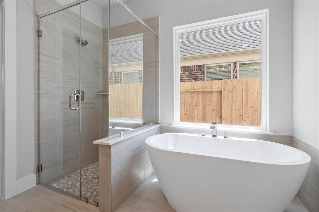 This additional view of the primary bath features the walk-in shower with pebble flooring and tile surround, soaking tub, and window allowing in natural lighting!