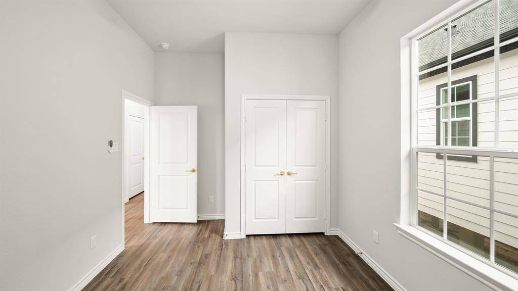 Bedroom features  ample natural light from a large window. It includes a double-door closet and an open doorway leading to another area, creating a bright and airy feel.