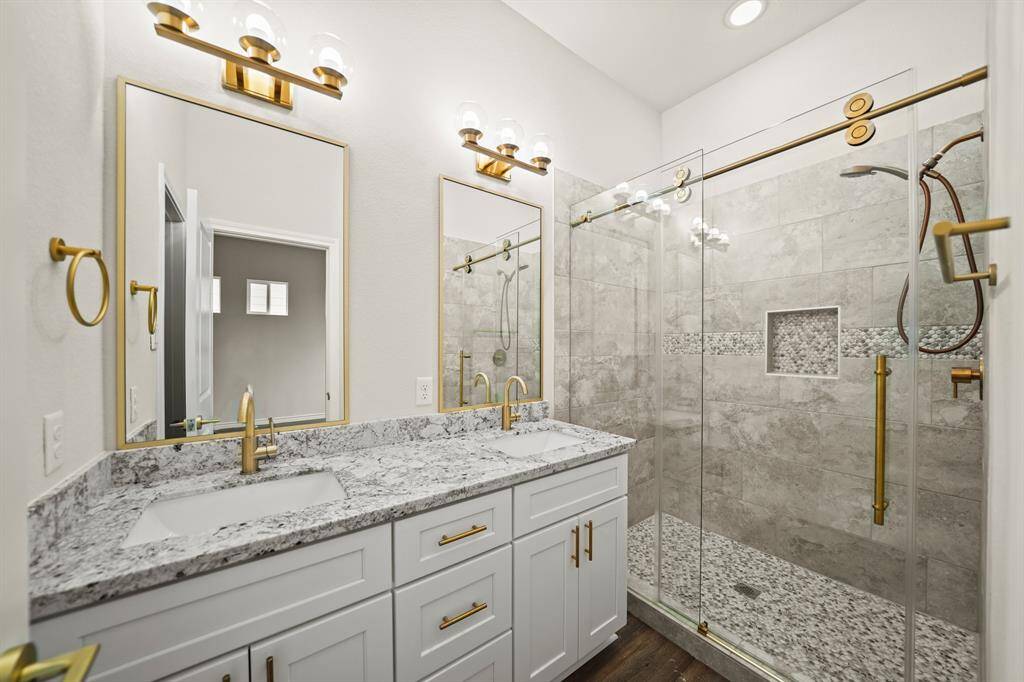 Indulge in luxury with this spa-like primary bathroom featuring sleek white cabinetry, elegant gold fixtures, and stunning granite countertops. The glass-enclosed walk-in shower, highlighted by intricate tilework, perfectly marries modern design with timeless elegance.