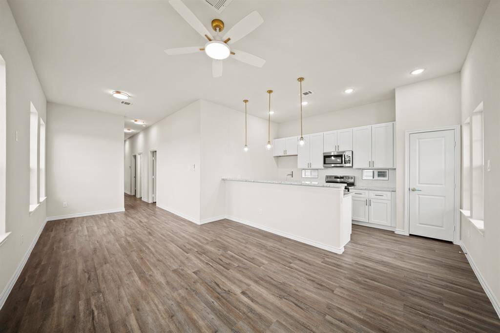 Open-concept living area with modern finishes. It features wood-look flooring, large windows, and a sleek kitchen with white cabinetry, stainless steel appliances, and pendant lighting. Perfect for contemporary living.