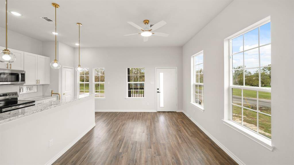 Bright and modern open-concept living area with large windows, hardwood floors, and a stylish kitchen featuring marble countertops and pendant lighting. Perfect for natural light and comfortable living.