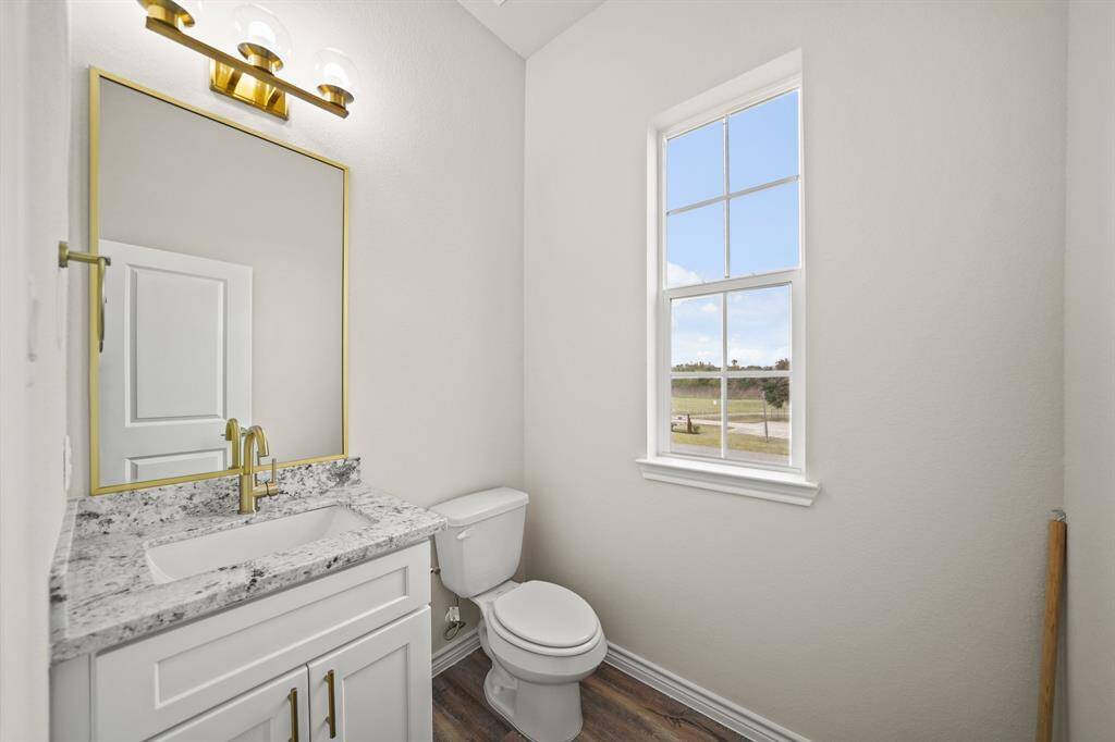 Half bathroom features a modern design with a granite countertop, white cabinetry, and gold  fixtures. A large window provides natural light, and the space has a clean, bright ambiance.