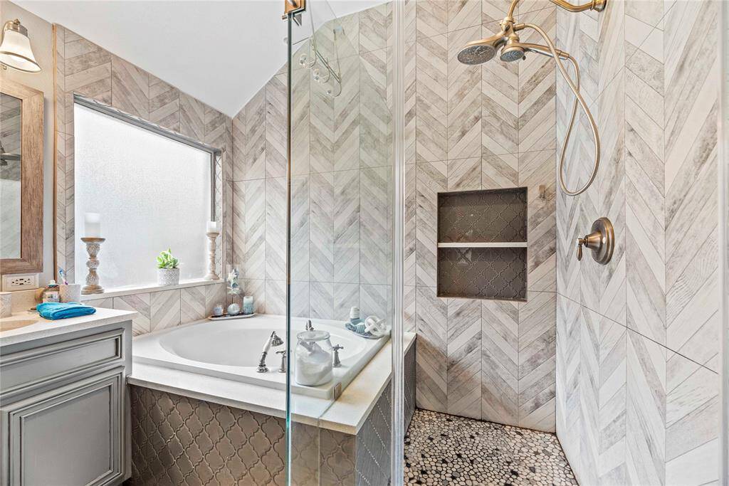 This ensuite bathroom features a luxurious frameless glass shower, complete with convenient shampoo ledges and upgraded fixtures for a true spa-like experience. The river-rock floor adds a touch of natural elegance, providing a soothing contrast to the sophisticated tile work. Every detail has been thoughtfully designed to create a tranquil and stylish retreat.