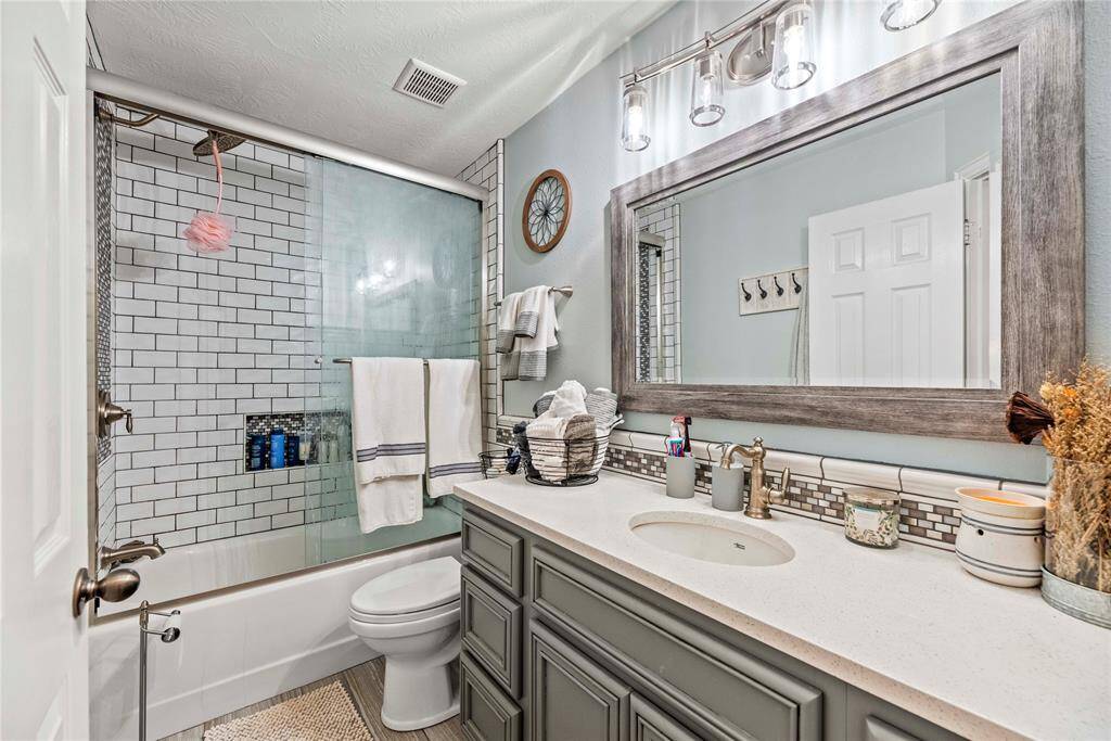 This beautiful full guest bathroom offers an extended vanity with ample storage below, featuring stunning tile work and a framed mirror with upgraded vanity lights above. The fully tiled tub/shower enclosure with a sliding glass door and upgraded fixtures adds a touch of luxury to the space. Every detail has been carefully chosen to create a stylish and functional bathroom for your guests.