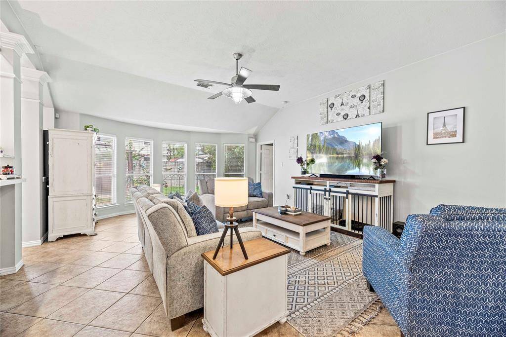 The spacious family room, with tile flooring and a modern fan, seamlessly connects to the kitchen and dining areas. Bathed in natural light from a wall of windows along the back, this room offers neutral finishes and ample space for everyone to gather comfortably. It's the perfect setting for family activities and entertaining guests.