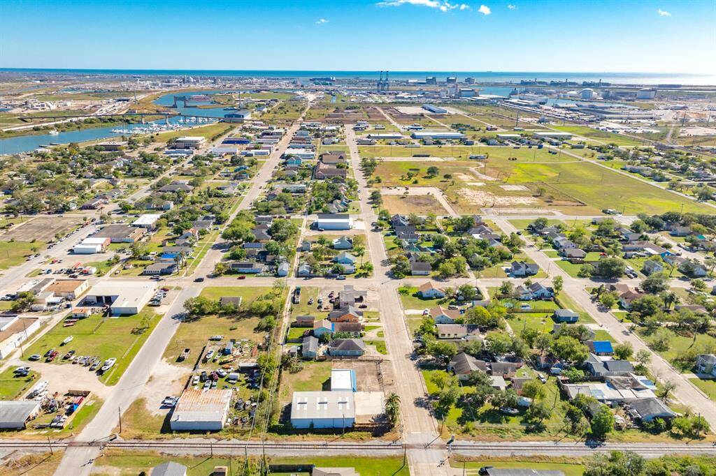 This aerial photo showcases a suburban neighborhood with a mix of residential homes, green spaces, and nearby waterways. The area appears peaceful, with well-laid-out streets and proximity to commercial facilities and a port or industrial area in the distance. Ideal for buyers seeking a blend of residential living and access to amenities.