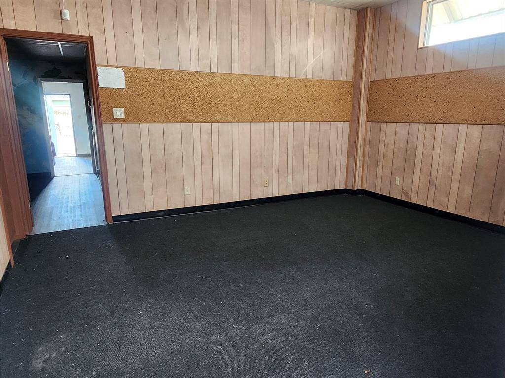 This room features wood paneling and a dark carpet. It has a small high window for natural light and an opening leading to another area with different flooring. Ideal for customization.