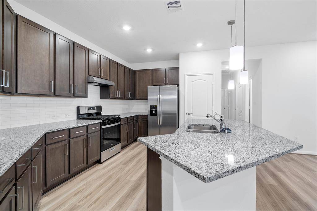 Another view of this beautiful kitchen showcasing the stainless steel Whirlpool gas range and refrigerator, and the granite countertop with modern tile backsplash.