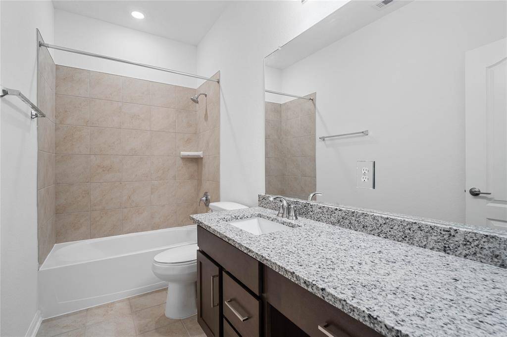 Secondary bath features tile flooring, bath/shower combo with tile surround, wood cabinets, beautiful granite countertops, mirror, dark, sleek fixtures and modern finishes.