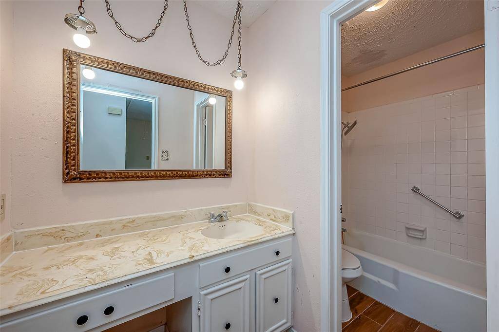 Has two bathrooms with a single vanity and a large mirror, featuring a bathtub/shower combo, wooden flooring, and overhead lighting.
