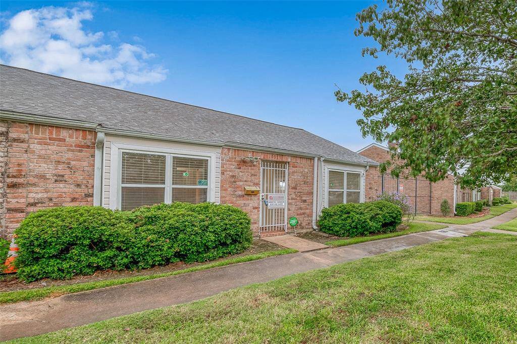 This is a well-maintained single-story townhouse featuring large windows, a secure entrance gate, and manicured landscaping. The community is quiet with a tidy walkway and green lawn.