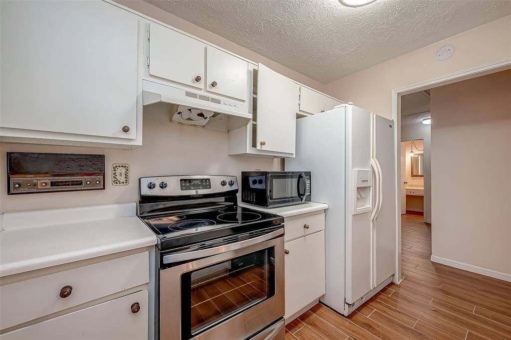 The kitchen features white appliances, including a refrigerator and an electric range, with traditional white cabinetry. It has laminate wood flooring and offers a view through to the next room, creating an open feel.