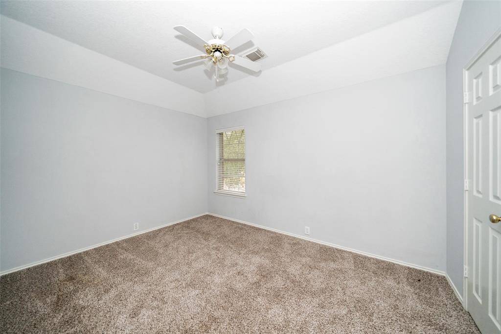 This is a bright, empty room with neutral walls, plush carpet, a window with blinds, and a ceiling fan, ideal for a bedroom or office.