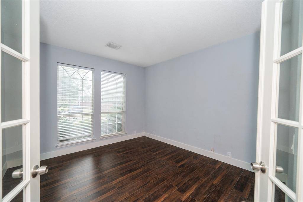 Bright room with two large windows and wooden floors, featuring light blue walls and white trim. French doors add elegance and natural light.