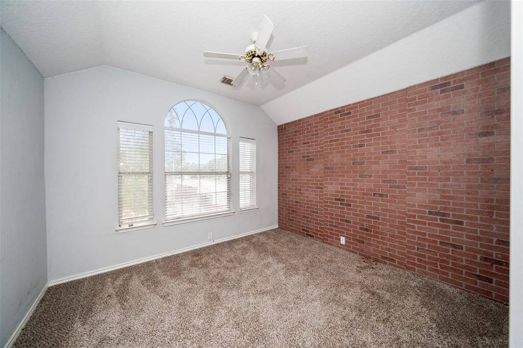 This room features a cozy carpeted floor, a stylish brick accent wall, and a large arched window that lets in plenty of natural light. The ceiling fan adds comfort and functionality.