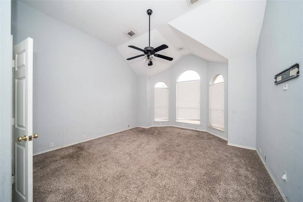This spacious room features vaulted ceilings, carpeted flooring, and large arched windows that provide ample natural light. A ceiling fan adds comfort, and the neutral walls offer a blank canvas for personalization.