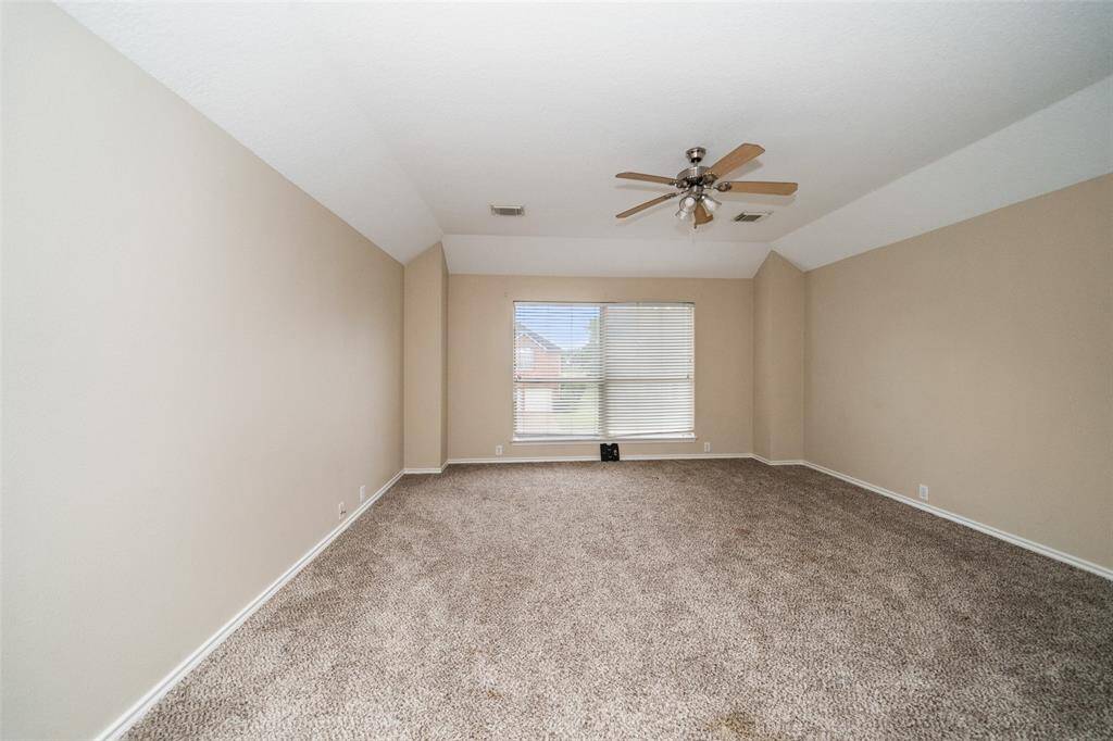 Spacious room with neutral walls, plush carpet, and a large window allowing natural light. Features a ceiling fan for comfort.