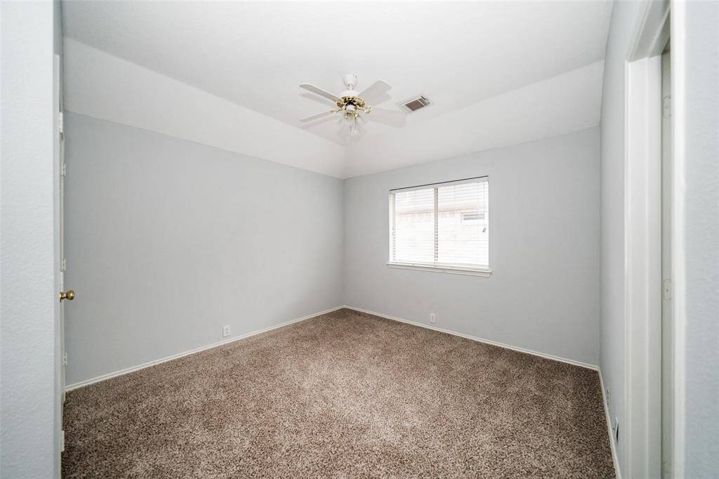 This is a bright, carpeted bedroom with neutral walls, featuring a ceiling fan and a window for natural light.