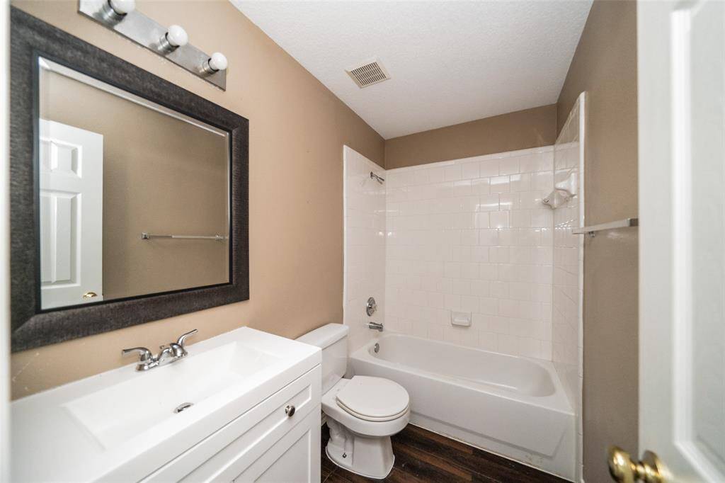 This bathroom features a modern vanity with a large mirror, a full bathtub with white tile surround, and a neutral color palette, offering a clean and functional space.