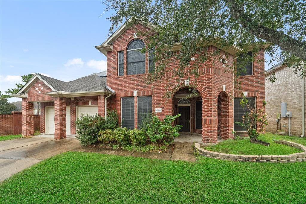 Charming two-story brick home with a welcoming front porch, arched windows, and a lush green lawn. The property features a spacious driveway and a cozy entryway, perfect for families seeking comfort and style.