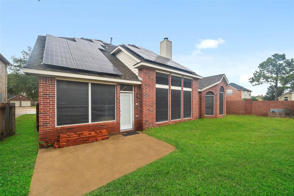 This photo showcases the exterior of a brick home with solar panels on the roof. It features large windows and a well-maintained backyard with a patio area. The setting is suburban, offering a sense of privacy with a fenced yard.
