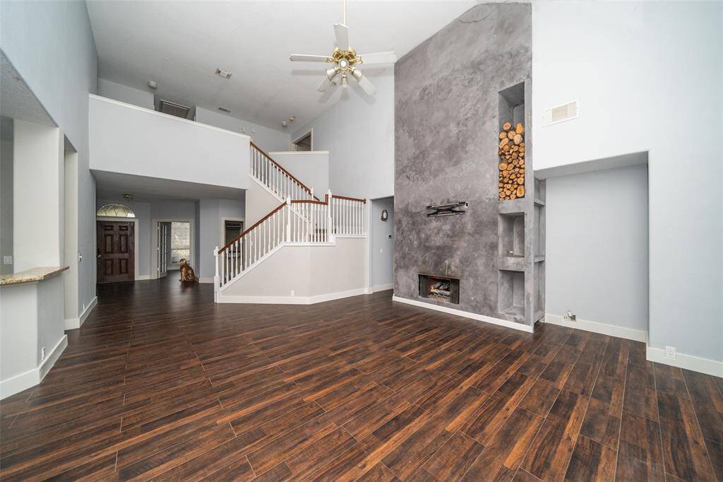 This spacious living room features high ceilings, dark hardwood floors, and a modern, minimalist fireplace with built-in wood storage. An elegant staircase leads to the second floor, creating an open and airy feel.