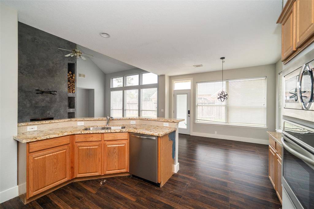 This photo showcases a bright, open kitchen with a modern, functional layout. It features granite countertops, wooden cabinetry, stainless steel appliances, and a breakfast bar. The space flows seamlessly into a living area with large windows and a contemporary fireplace, providing ample natural light and a welcoming atmosphere.