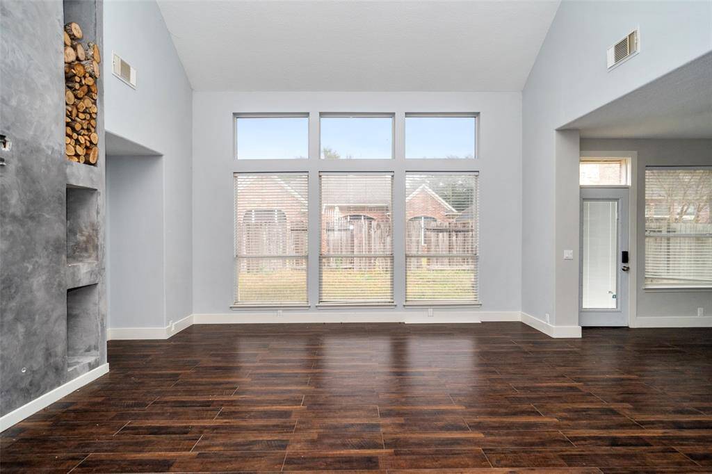 This spacious living area features high ceilings and large windows that provide plenty of natural light. The dark wood flooring adds a touch of elegance, and the built-in shelving offers convenient storage. The view of the backyard through the windows enhances the open feel of the room.