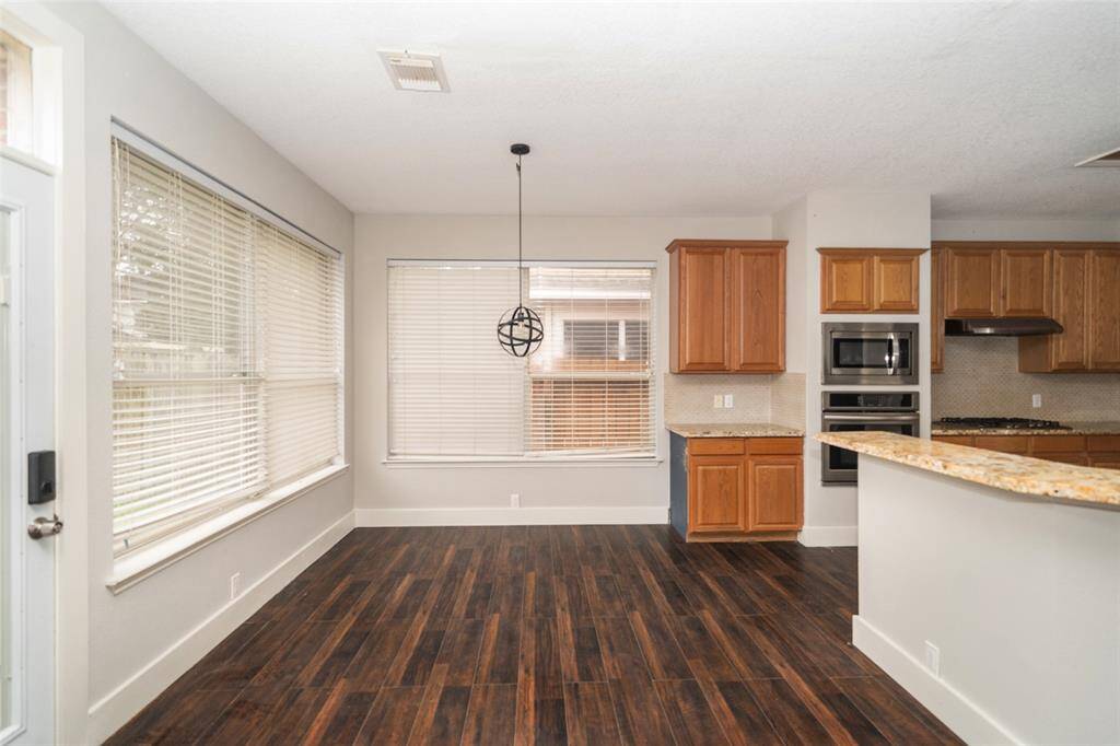 Bright kitchen space with large windows, hardwood flooring, and wooden cabinetry. Features a modern pendant light, granite countertops, and stainless steel appliances. Perfect for dining and entertaining.