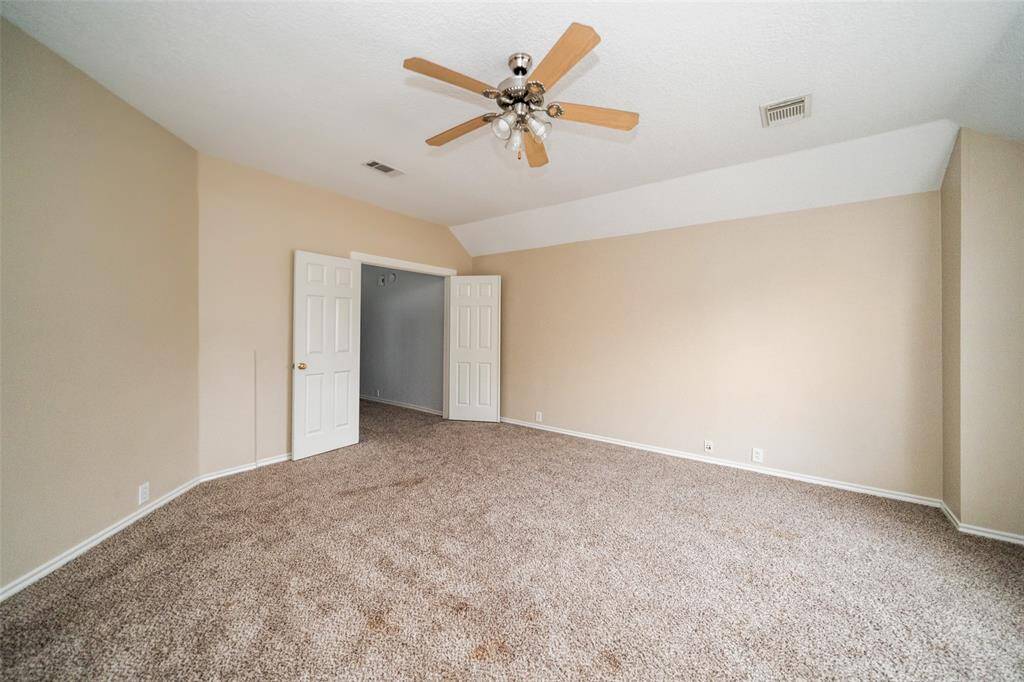 Spacious room with neutral walls and plush carpet, featuring a ceiling fan and double doors for easy access.