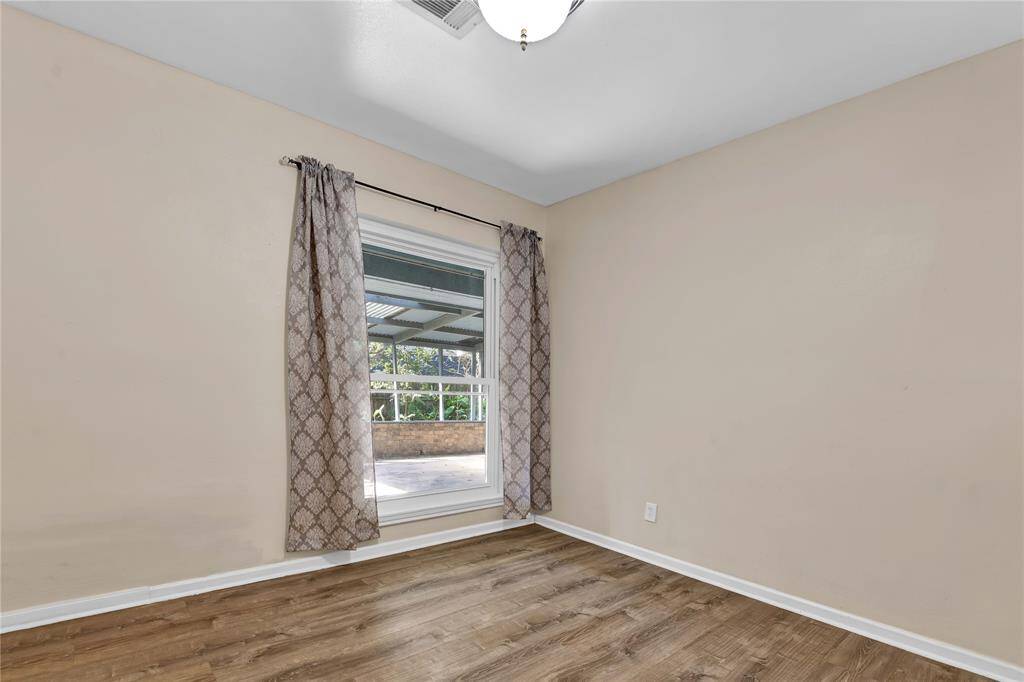 This room features neutral walls, hardwood flooring, and a large window offering a view of the patio. It's bright and versatile, ideal for various uses.