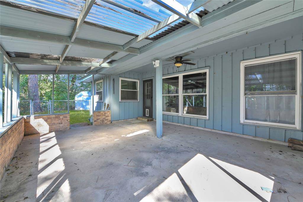 Spacious covered patio with a concrete slab and a partially transparent roof. The area is surrounded by a low brick wall, offering a view of the backyard. A ceiling fan is installed for added comfort.