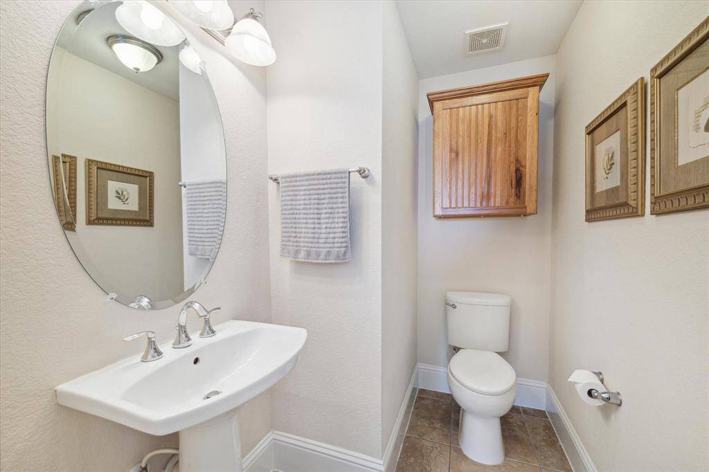 This half bath, situated off the living room area, features clean and modern finishes. The space is highlighted by a sleek pedestal sink with chrome fixtures and an oval mirror.