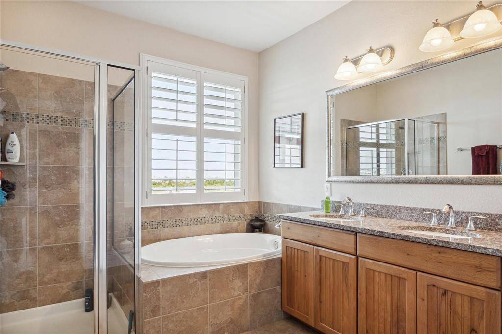 The master bathroom exudes luxury with its modern finishes, including a spacious walk-in shower, a relaxing soaking tub, and a double vanity with granite countertops. Beautiful tilework throughout, along with plantation shutters, enhances the peaceful ambiance of this spa-like retreat, with stunning water views just outside.