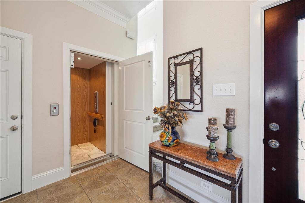 Luxury meets convenience in this elegant entryway featuring a private elevator, ensuring effortless access to all levels of the home. Ceramic tile flooring, crown molding, and a thoughtfully designed space create a warm and inviting atmosphere that sets the tone for the rest of the property.