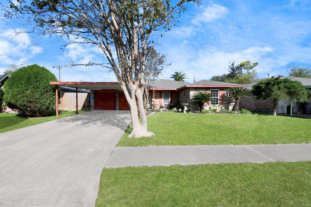 A welcoming view of the home's front yard featuring a carport and ample space for parking. The house’s exterior is well-maintained, with an inviting appearance.